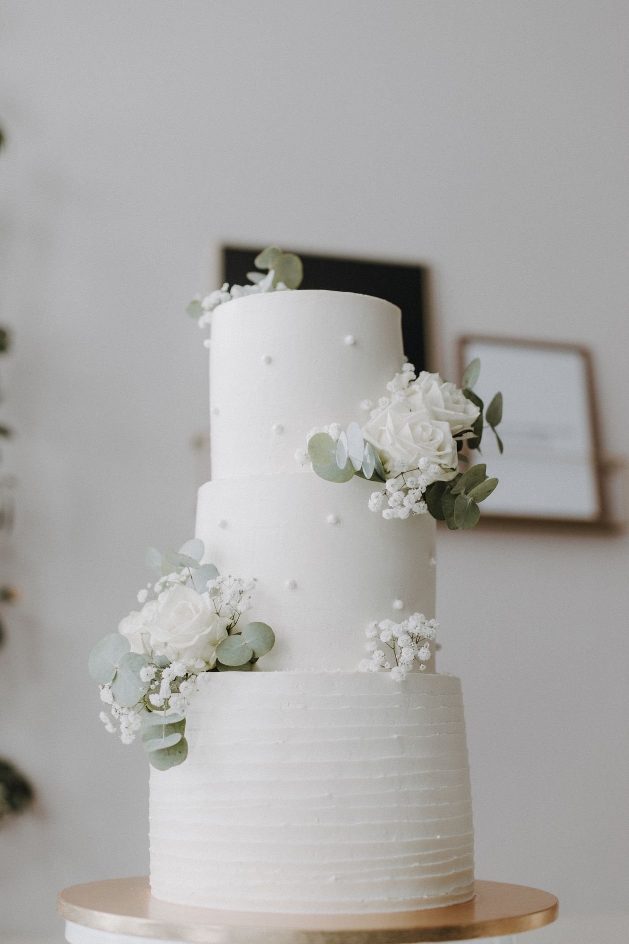 Three-tier white wedding cake decorated with white roses and eucalyptus